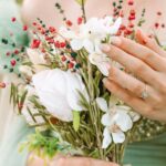 Elegant hand with manicured nails holding a bouquet of white flowers and red berries at Golden Rose Nail Studio, showcasing bridal or special occasion nail designs and floral accessories.