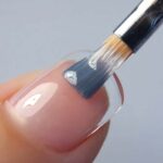 Polished nail with clear gel polish and brush applying top coat at Golden Rose Nail Studio.