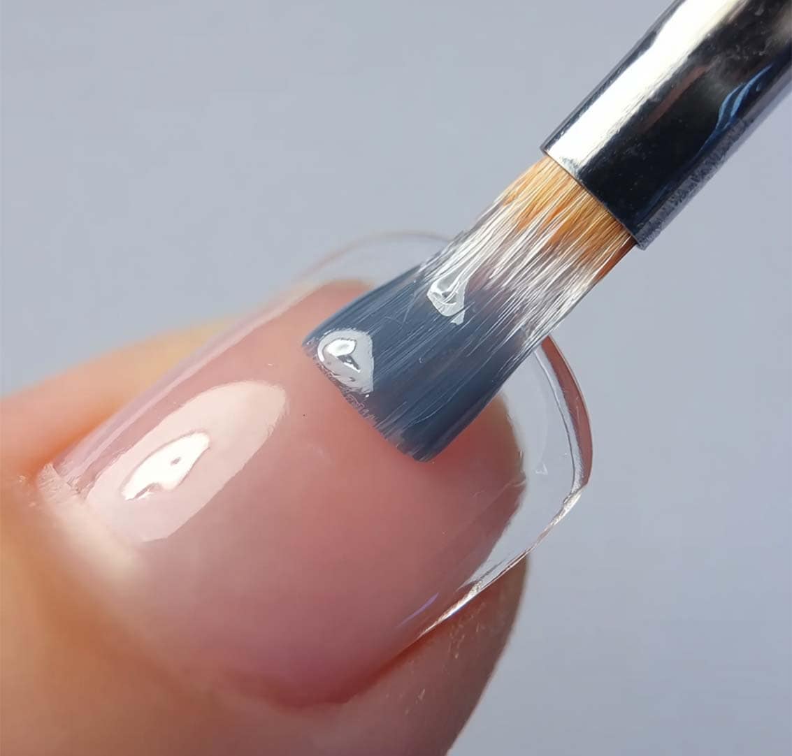 Polished nail with clear gel polish and brush applying top coat at Golden Rose Nail Studio.